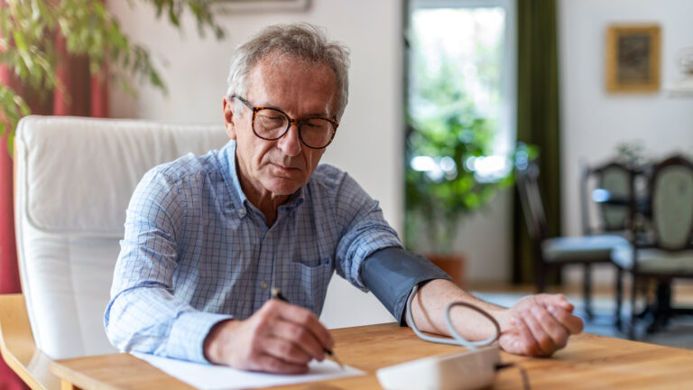 Mann macht sich Notizen während er am Tisch sitzt und Blutdruck misst.