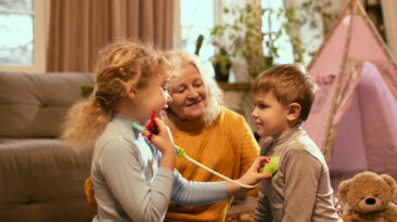 Children enthusiastically perform pretend health check-up with toy medical tools, guided by grandmother nurturing curiosity about medical care. Concept of knowledge about healthy lifestyle, medicine.