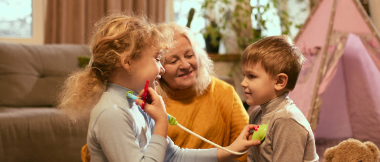 Children enthusiastically perform pretend health check-up with toy medical tools, guided by grandmother nurturing curiosity about medical care. Concept of knowledge about healthy lifestyle, medicine.