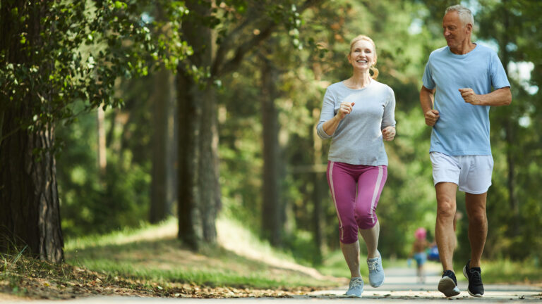 Active and healthy aged couple running in natural environment on summer morning