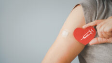 senior woman holding red heart shape with syringe and showing her arm with bandage after got vaccinated or inoculation due to spread of corona virus, population, social or herd immunity concept