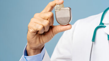 Portrait of professional doctor, cardiologist holding pacemaker selective focus on hands, closeup standing isolated on blue background. Treatment, cardiology concept