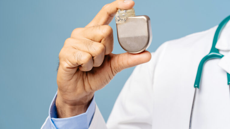 Portrait of professional doctor, cardiologist holding pacemaker selective focus on hands, closeup standing isolated on blue background. Treatment, cardiology concept