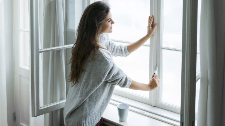 Woman is opening window to look at beautiful snowy landscape outside