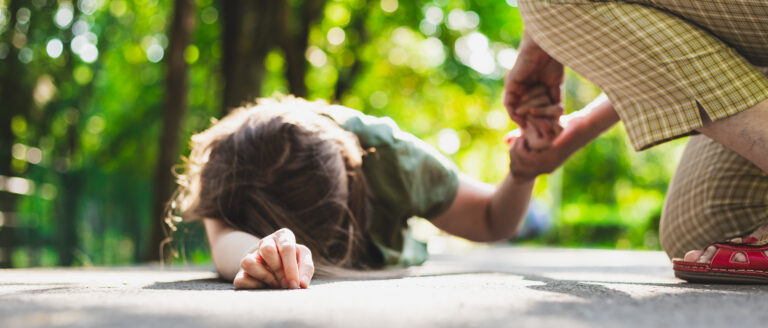 Fainted girl helped by an old woman – Teenager lying on the ground while receiving support from an elder