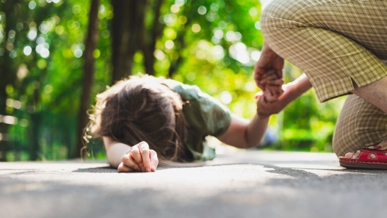 Fainted girl helped by an old woman – Teenager lying on the ground while receiving support from an elder